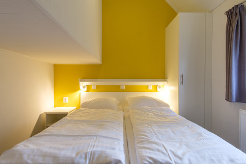 Slaapkamer in Vechtdallodge, Kampeerdorp de Zandstuve, Nederland, met twee eenpersoonsbedden en gele muur.
