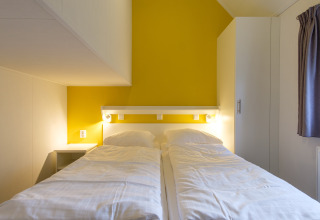 Soveværelse i Vechtdallodge på Kampeerdorp de Zandstuve, Holland, med to enkeltsenge og gult vægpanel.