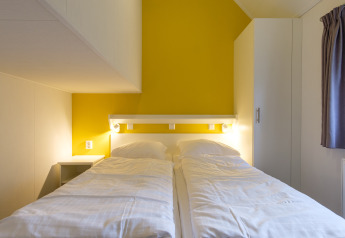 Chambre à la Vechtdallodge au Kampeerdorp de Zandstuve, Pays-Bas, avec deux lits jumeaux et mur jaune.