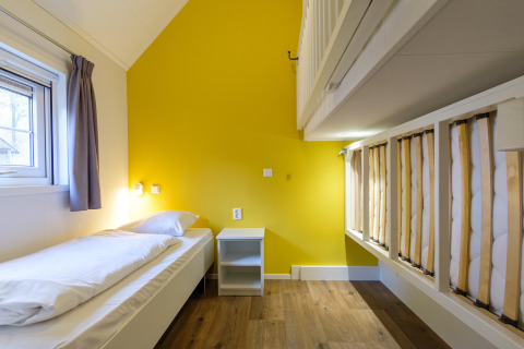 Heldere, moderne slaapkamer met eenpersoonsbed, stapelbed, gele muur en houten vloer bij Vechtdallodge.