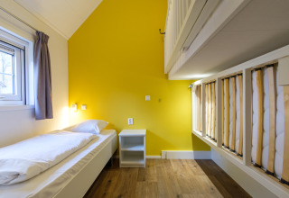 Dormitorio luminoso y moderno con cama individual, litera, pared amarilla y suelo de madera en Vechtdallodge.