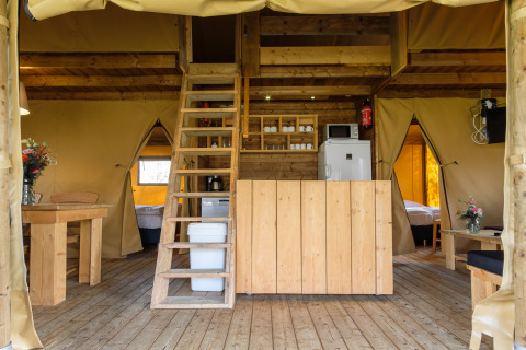 Interior de la tienda safari Verandalodge en Kampeerdorp de Zandstuve con muebles de madera y altillo.