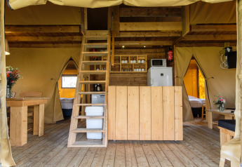 Interno della tenda safari Verandalodge al Kampeerdorp de Zandstuve con arredi in legno e soppalco.
