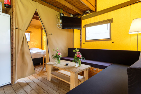 Vista interior de la acogedora tienda safari Verandalodge con sala de estar y dormitorio en Kampeerdorp de Zandstuve, Países Bajos.