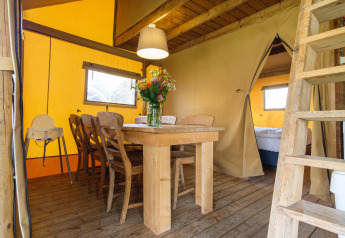 Vista interna della tenda safari Verandalodge con tavolo da pranzo a Kampeerdorp de Zandstuve, Paesi Bassi.