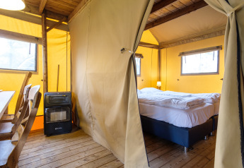 Interior view of a Verandalodge safari tent with bed, wooden chairs and heater at Kampeerdorp de Zandstuve.