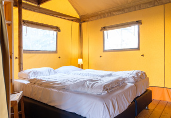 Komfortables Bett in einem Verandalodge-Safarizelt bei Kampeerdorp de Zandstuve, Niederlande, mit Holzfußboden.