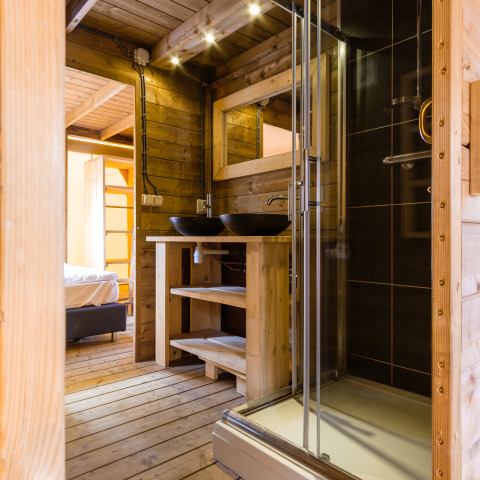 Modern wooden bathroom with glass shower and double sinks in Verandalodge safari tent, Netherlands.