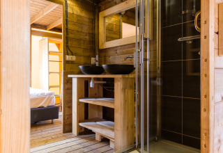 Modern wooden bathroom with glass shower and double sinks in Verandalodge safari tent, Netherlands.