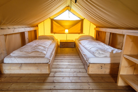 Indretning af safaritelt Verandalodge med to senge, trægulv og hyggelig belysning i Kampeerdorp de Zandstuve.