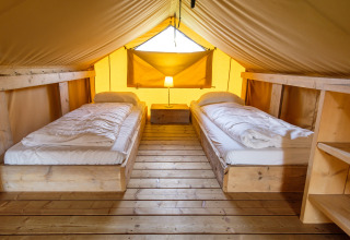 Intérieur de la tente safari Verandalodge avec deux lits et plancher en bois à Kampeerdorp de Zandstuve.