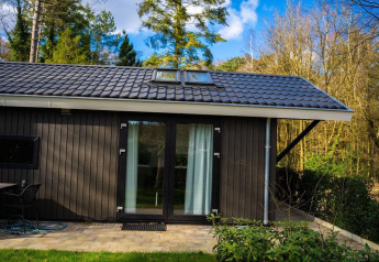 Udsigt til Bos Cottage-lodge ved De Thijmse Berg i Holland, omgivet af frodig skov og blå himmel.