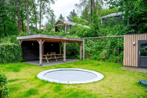 Jardín familiar con trampolín, columpios y zona de picnic cubierta en Wellness Cottage 6p en De Thijmse Berg, Países Bajos.