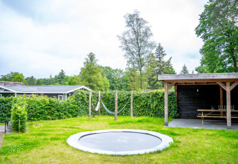 Udendørs have med indbygget trampolin, hængekøje og overdækket terrasse i Wellness Cottage på De Thijmse Berg.