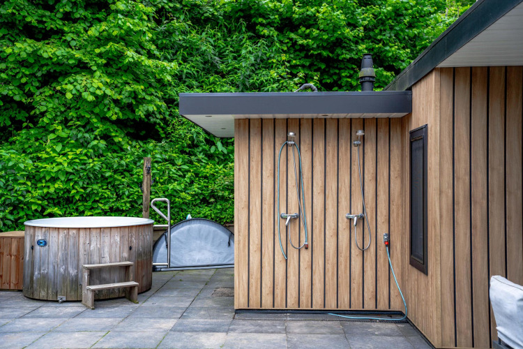 Área de bienestar al aire libre con bañera de madera y duchas en Wellness Cottage 6p en De Thijmse Berg, Países Bajos.
