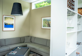 Moderne stue med grå hjørnesofa, kunst på væggene og hylder med glas i Wellness Cottage 6p, Nederländerne.
