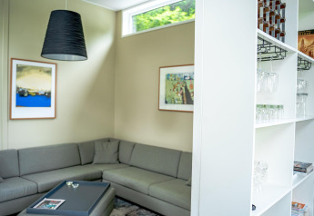 Moderne stue med grå hjørnesofa, kunst på væggene og hylder med glas i Wellness Cottage 6p, Nederländerne.