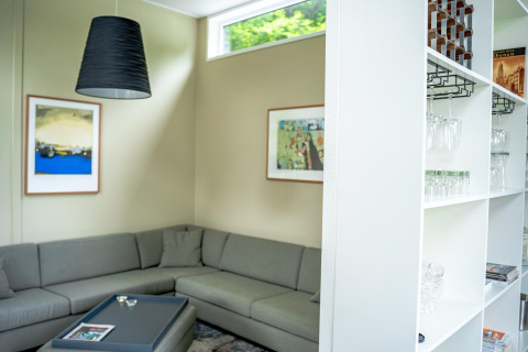 Moderne zithoek met grijze hoekbank, kunstwerken en glazen kast in Wellness Cottage 6p, Nederland.