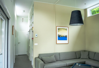 Salon moderne du Wellness Cottage 6p à De Thijmse Berg aux Pays-Bas avec canapé d’angle gris et décoration murale.