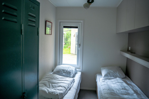 Habitación luminosa con dos camas individuales, ventana y taquilla en Wellness Cottage 6p, Países Bajos.