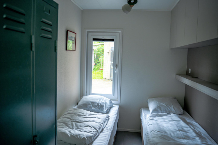 Habitación luminosa con dos camas individuales, ventana y taquilla en Wellness Cottage 6p, Países Bajos.