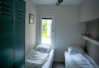 Habitación luminosa con dos camas individuales, ventana y taquilla en Wellness Cottage 6p, Países Bajos.