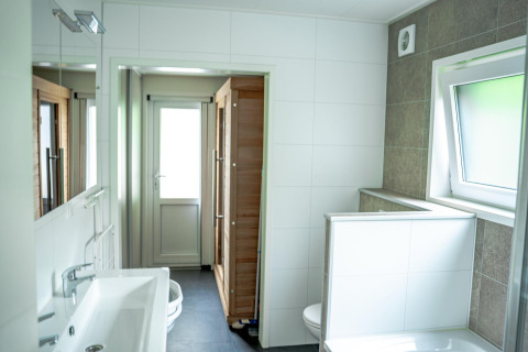 Baño moderno con lavabo grande, espejo, inodoro separado y ventana en Wellness Cottage 6p, De Thijmse Berg, Países Bajos.