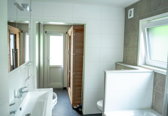 Moderne badeværelse med håndvask, spejl, delvist opdelt toilet og store vinduer i Wellness Cottage 6p, De Thijmse Berg.