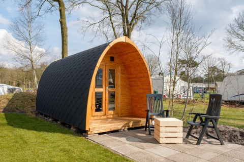 Cabaña de madera tipo pod con terraza y sillas en Kampeerdorp de Zandstuve, Países Bajos, al aire libre.