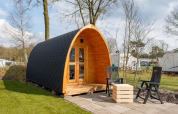 Cabaña de madera tipo pod con terraza y sillas en Kampeerdorp de Zandstuve, Países Bajos, al aire libre.