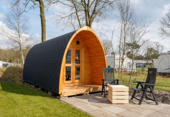 Gemütliche Holz-Pod-Unterkunft mit kleiner Veranda und Stühlen bei Kampeerdorp de Zandstuve, Niederlande.