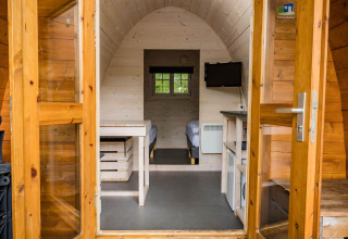 Ingang van een houten pod met twee bedden, tv en keukenhoek bij Kampeerdorp de Zandstuve, Nederland.