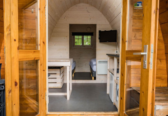 Entrance view of a wooden pod with two beds, TV and kitchenette at Kampeerdorp de Zandstuve, Netherlands.