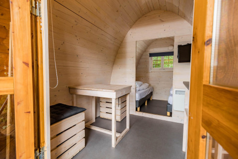 Innenansicht einer gemütlichen Pod-Hütte mit Holzwänden, Schreibtisch und Bett in Kampeerdorp de Zandstuve, Niederlande.