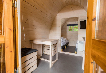 Vista interna di un’accogliente pod con pareti in legno, scrivania e letto a Kampeerdorp de Zandstuve, Paesi Bassi.