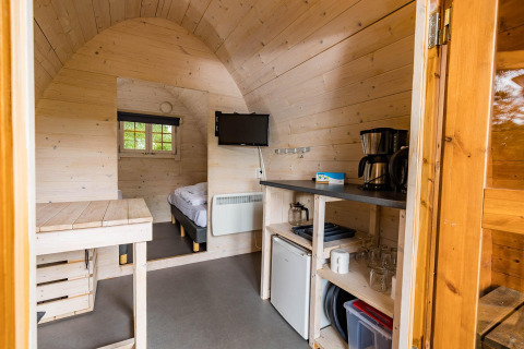 Vista interior de un acogedor pod en Kampeerdorp de Zandstuve, Países Bajos, con cama y pequeña cocina.