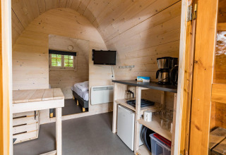 Vista interior de un acogedor pod en Kampeerdorp de Zandstuve, Países Bajos, con cama y pequeña cocina.
