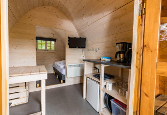 Indvendigt billede af en hyggelig pod på Kampeerdorp de Zandstuve i Holland med seng, tekøkken og TV.
