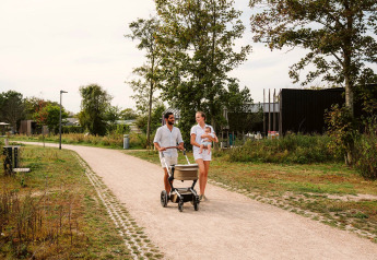 Eine Familie spaziert auf dem Weg mit Kinderwagen und Baby im Arm bei einer Glamping-Unterkunft.