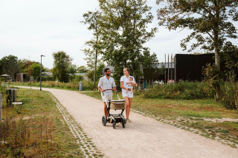 Gezin wandelt samen met kinderwagen en baby op arm op een pad bij een glamping accommodatie in de natuur.