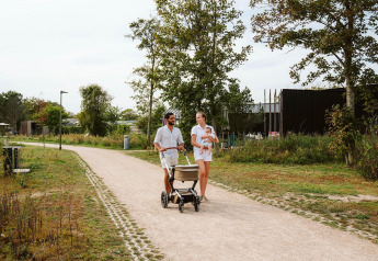 Gezin wandelt samen met kinderwagen en baby op arm op een pad bij een glamping accommodatie in de natuur.