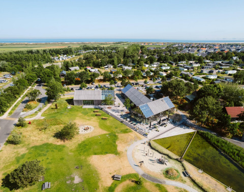 Luchtfoto van een moderne glamping accommodatie met groene zones, huisjes en gemeenschappelijke gebouwen bij zee.
