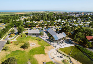 Vista aérea de alojamiento glamping moderno con áreas verdes, casas y edificios comunes cerca del mar.