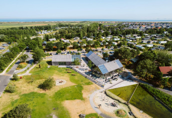 Vista aerea di un moderno alloggio glamping con spazi verdi, cabine e aree comuni vicino al mare.