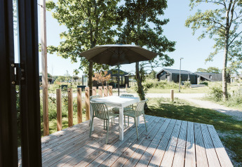 Udendørs træterrasse med bord, fire stole og parasol ved Klaproos tiny house, De Klepperstee, Holland.