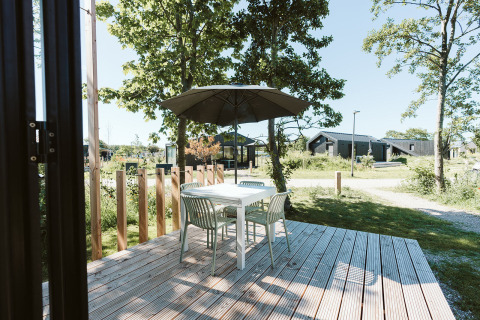 Wooden patio with table, four chairs, and umbrella at Klaproos tiny house, De Klepperstee, Netherlands.