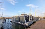 Houseboat named Havenlodge Lelystad docked at Marina Parcs Lelystad in the Netherlands on a clear day.
