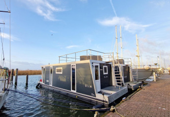 Hausboot Havenlodge Lelystad liegt am Steg im Marina Parcs Lelystad, Niederlande, bei sonnigem Wetter.