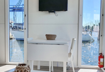 Interiør af houseboat Havenlodge Lelystad med bord, stol, tv og udsigt over marinaen i Nederlandene.