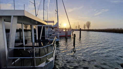 Solnedgang over vandet ved Havenlodge Lelystad i Marina Parcs Lelystad, Holland, med husbåd og lystbåde.